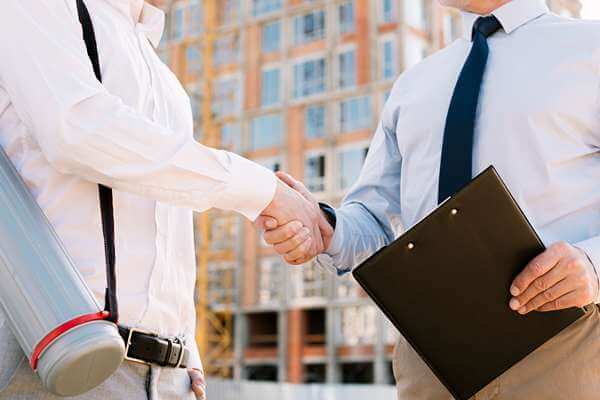 Two professionals shaking hands with an under-construction building in the background, symbolizing collaboration in joint development projects